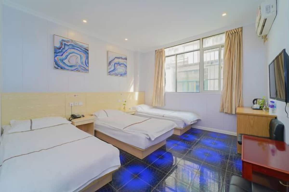 A hotel room with three beds, a desk, a TV, and artwork on the walls.