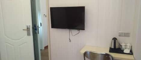 A room with a white door, a flat-screen TV mounted on the wall, a small table with a chair, and a mirror.