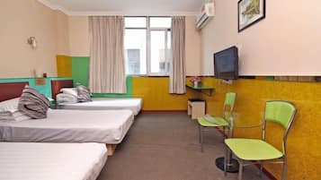 Quarto de hotel com três camas de solteiro, uma mesa com cadeira, televisão e janela com cortinas.