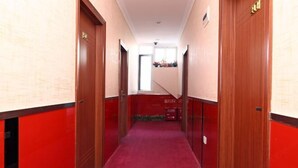 A hallway with red carpet and wooden doors, leading to a room with a window and a small plant. - Xiangfu Hostel (Shanghai Wuning Road) (Shanghai)