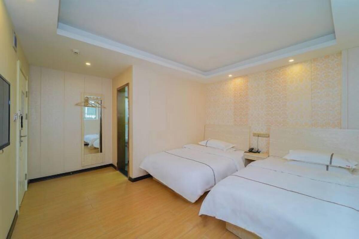 A hotel room with two beds, a wardrobe, a mirror, and a television.