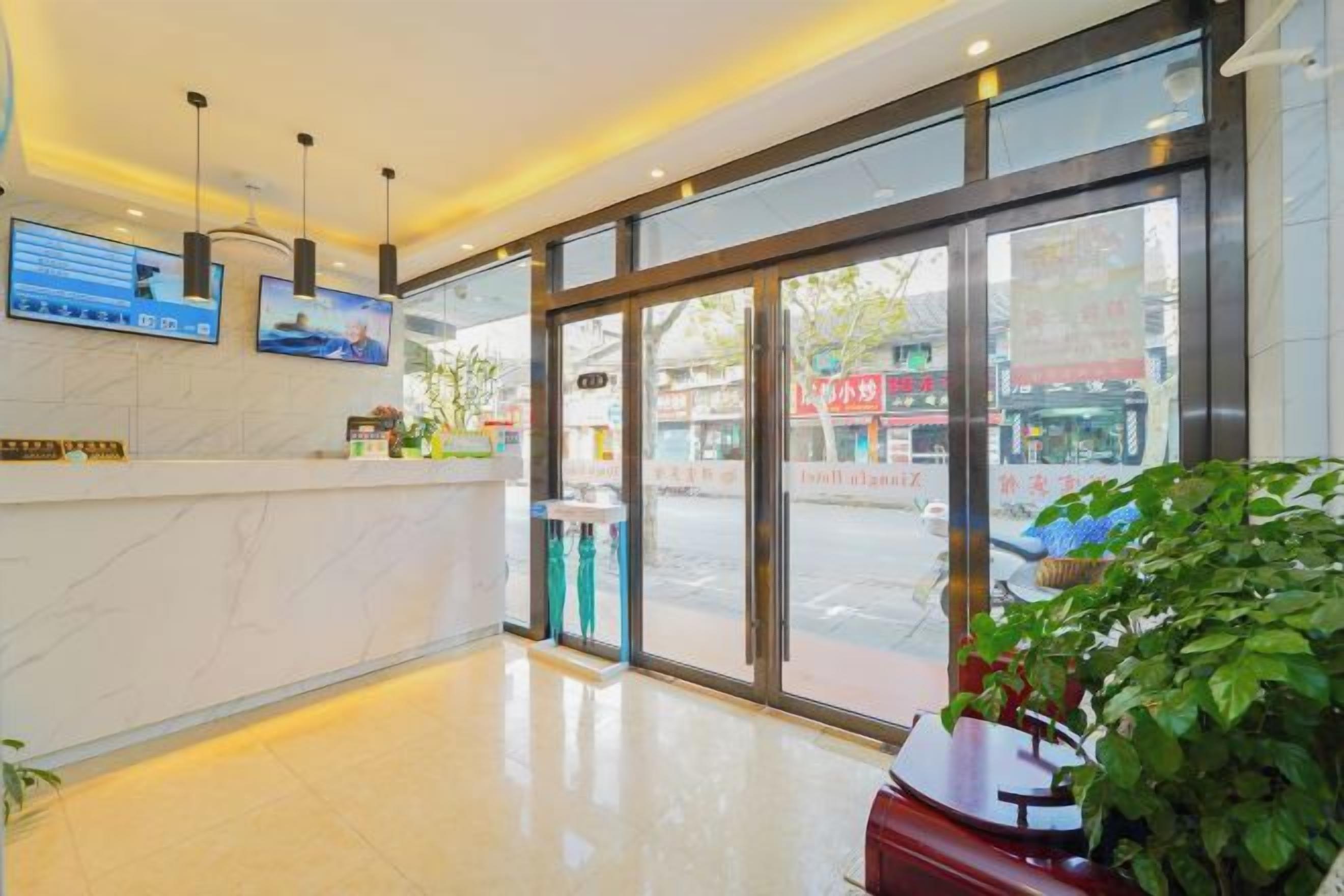 Uma área de recepção de hotel com balcão de mármore, grandes portas de vidro e vista para a rua.