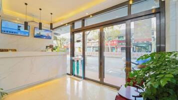 Uma área de recepção de hotel com balcão de mármore, grandes portas de vidro e vista para a rua.