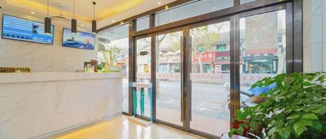 A hotel reception area with a marble counter, large glass doors, and a view of the street outside.