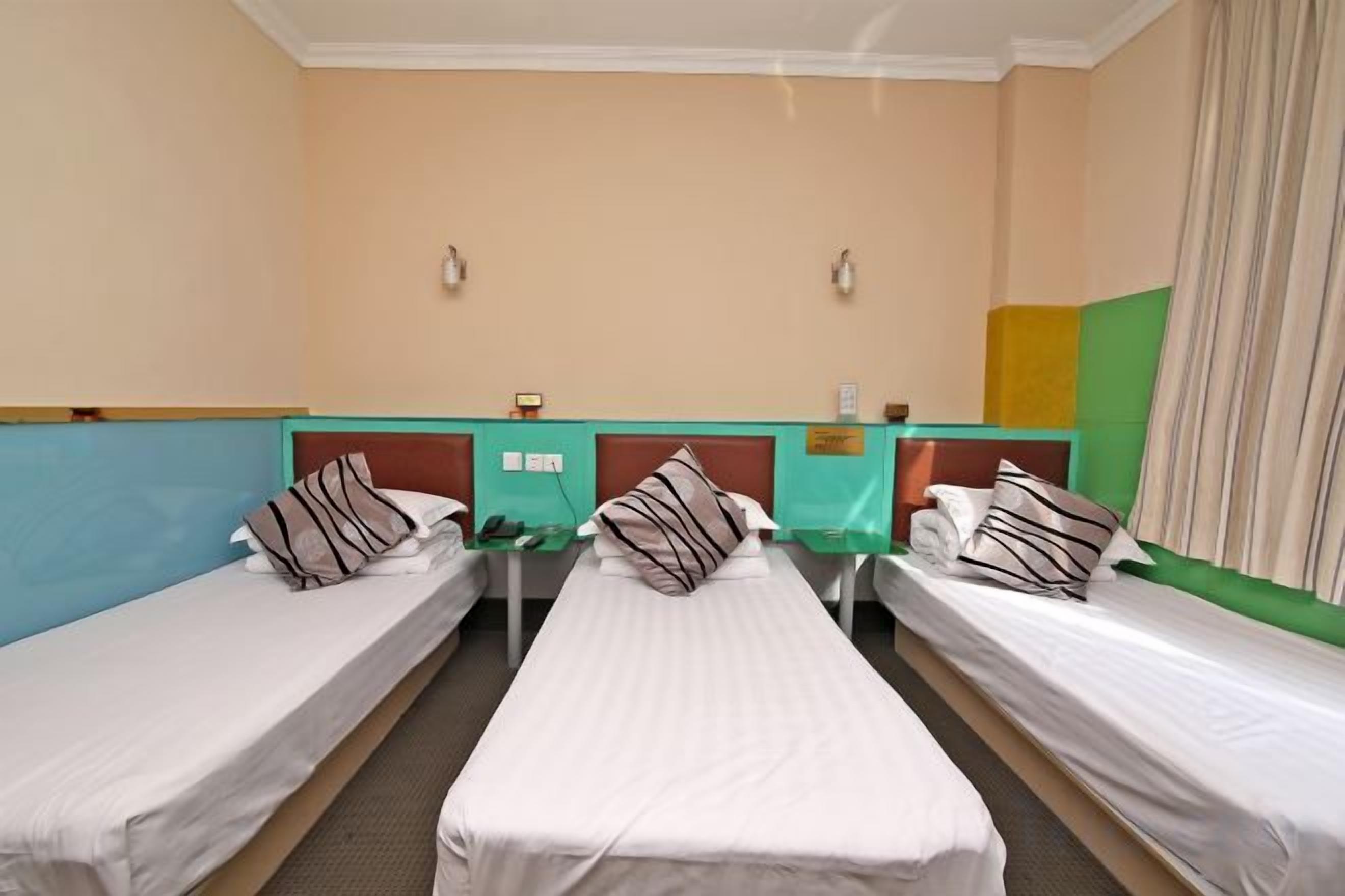 Quarto de hotel com três camas de solteiro, uma mesinha e um balcão verde.