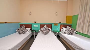 Quarto de hotel com três camas de solteiro, uma mesinha e um balcão verde.