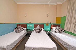 Quarto de hotel com três camas de solteiro, uma mesinha e um balcão verde.