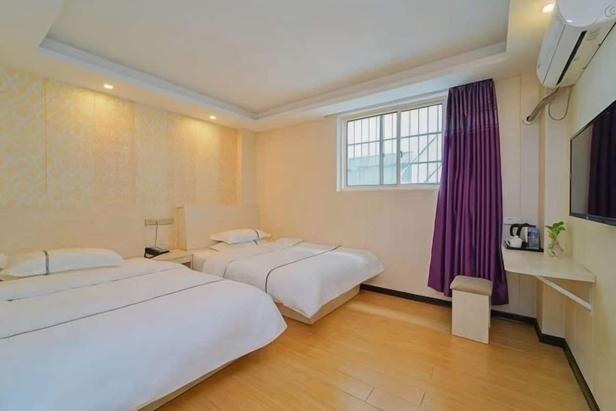 A hotel room with two beds, a desk, a window with curtains, and an air conditioning unit.