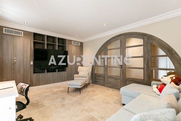 A spacious living room with a large arched window, a comfortable sofa, a chair, a television, and built-in shelving.