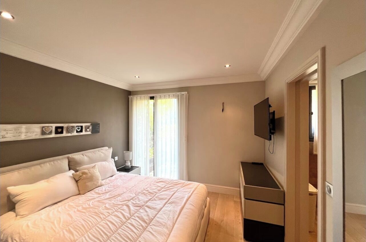 Une chambre à coucher avec un lit, un téléviseur fixé au mur, une table de chevet et une fenêtre avec des rideaux.