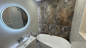 A modern bathroom with a freestanding bathtub, a round mirror with underglow lighting, and a wall with a leaf pattern. - Apartament with sea wiev (Nice)