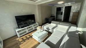A modern living room with a large flat-screen TV, a sofa, a coffee table, and a dining area with a table and chairs. - Apartament with sea wiev (Nice)