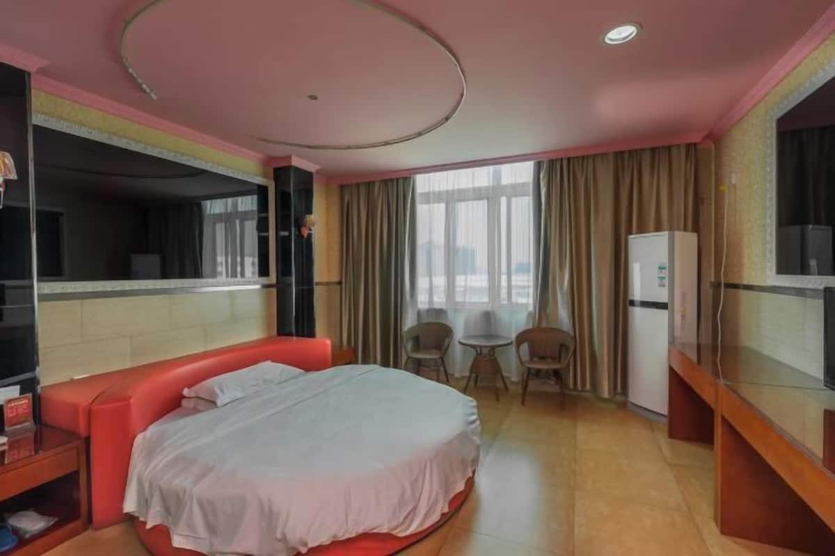Quarto de hotel com cama, televisão, frigorífico e uma pequena mesa com cadeiras.