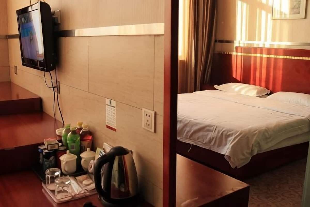 Quarto de hotel com cama, televisão na parede, mesa pequena com produtos de higiene e janela com cortinas.