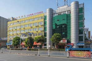 A multi-story building with a yellow facade and green windows, surrounded by trees and a blue vehicle. - Wuhu Tiandu Express Hotel (Wuhu)
