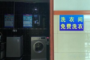 A laundry facility with a washing machine and a sign indicating free laundry services. - Wuhu Tiandu Express Hotel (Wuhu)