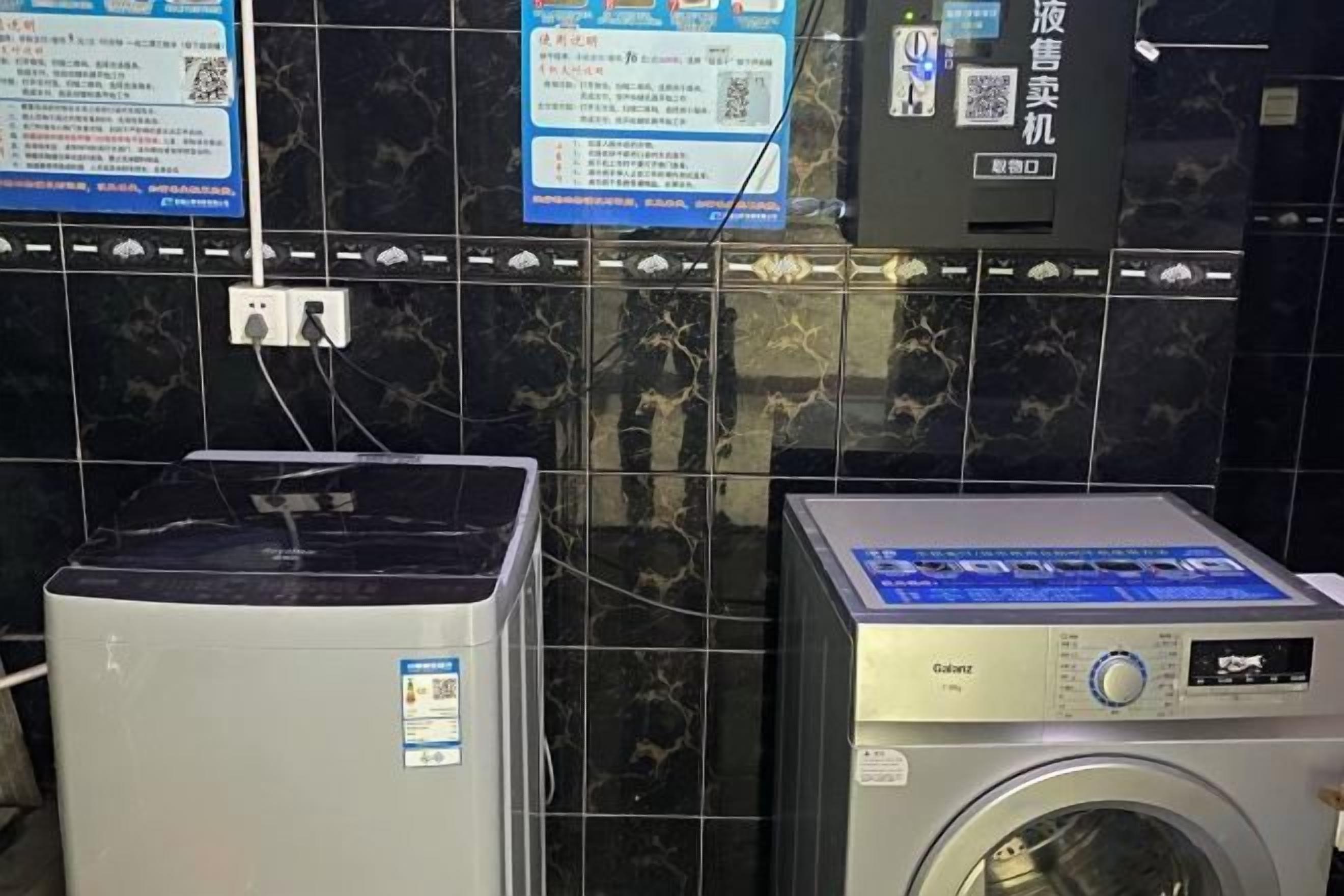 A laundry area with a washing machine and dryer, a wall-mounted control panel, and a QR code for digital information.