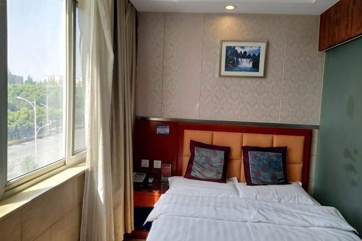 Quarto de hotel com cama, mesa de cabeceira, janela com cortinas, um quadro na parede e vista para o exterior.