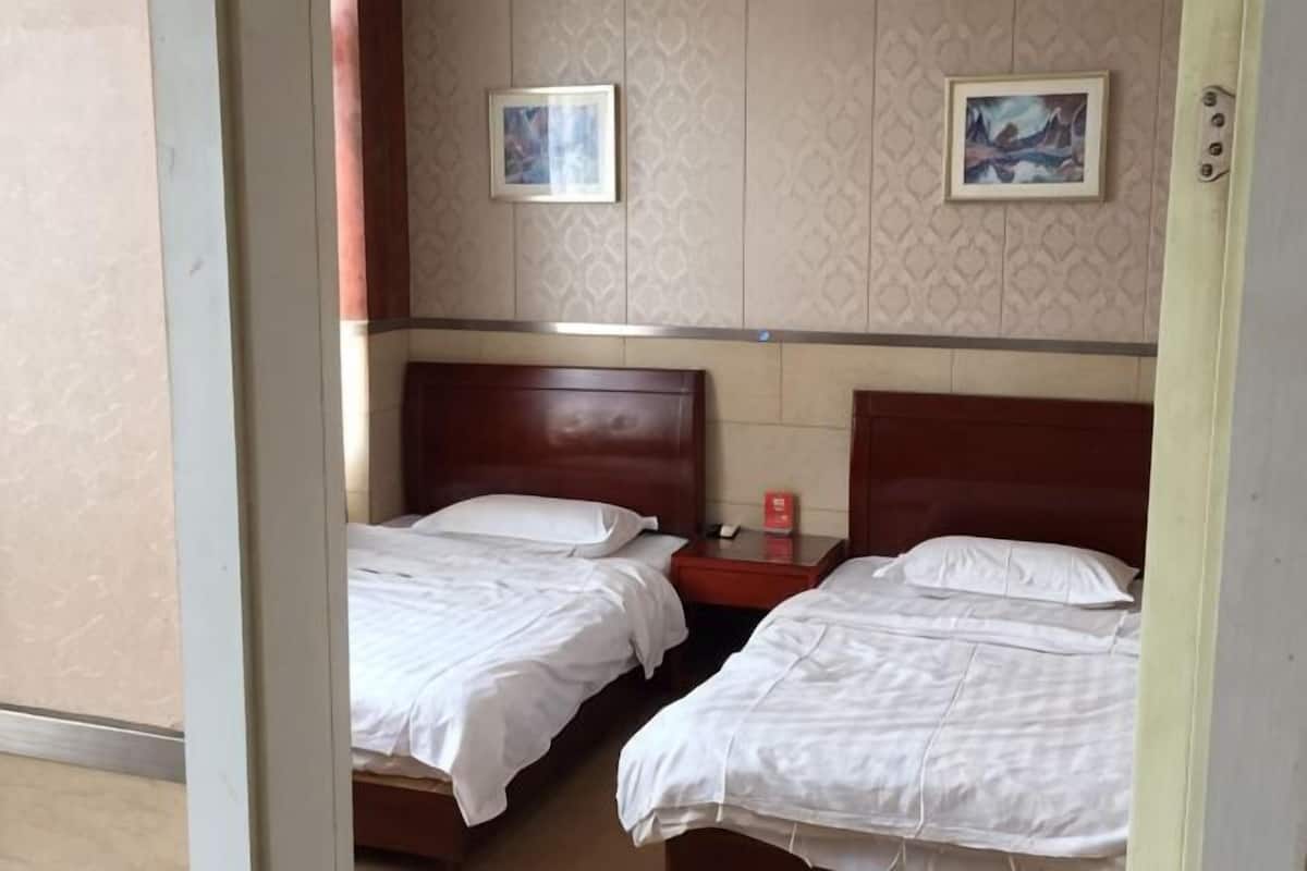 Quarto de hotel com duas camas, uma cabeceira de madeira, um criado-mudo e dois quadros na parede.