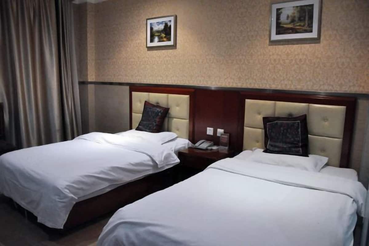 Quarto de hotel com duas camas de solteiro, cabeceira de madeira, mesa de cabeceira com abajur e duas fotografias emolduradas na parede.