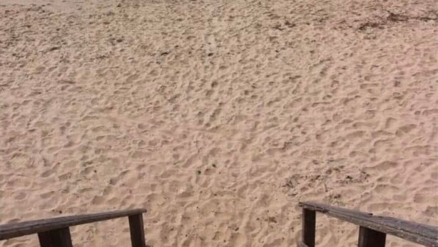 Une plage de sable avec une barrière en bois au premier plan.