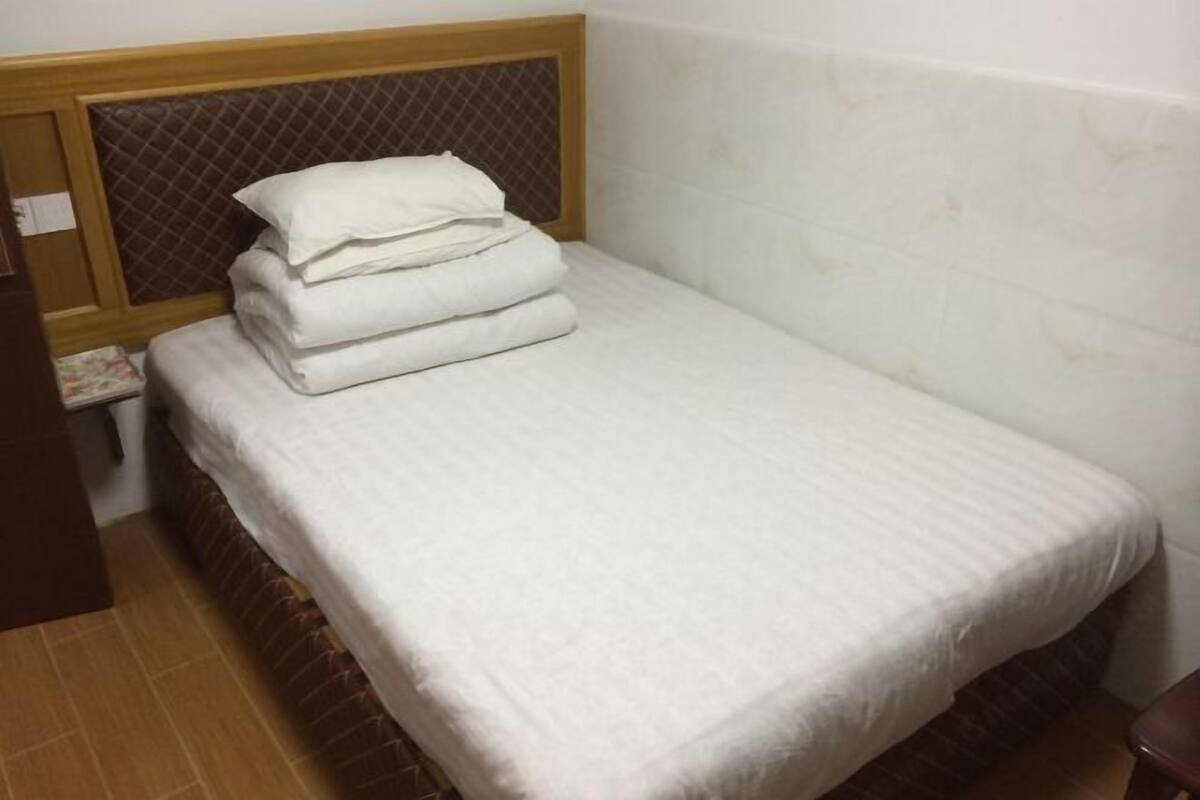 A small, neatly made bed with a white bedspread and pillows, a wooden headboard, and a tiled wall.