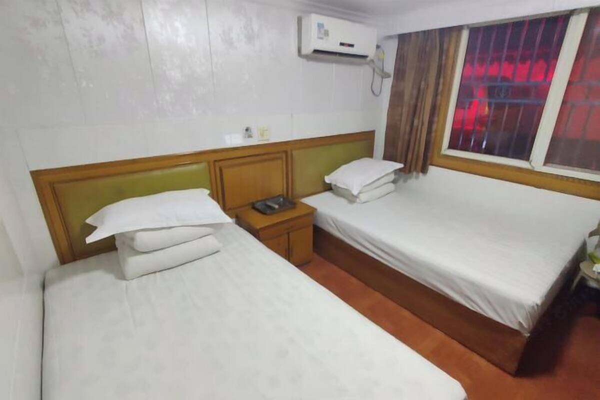 A hotel room with two beds, a wooden headboard, a bedside table with a phone, and an air conditioning unit.