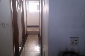 A narrow hallway with a tiled floor, a door on the left, and a light switch on the wall. - Jinying Hostel (Shanghai)