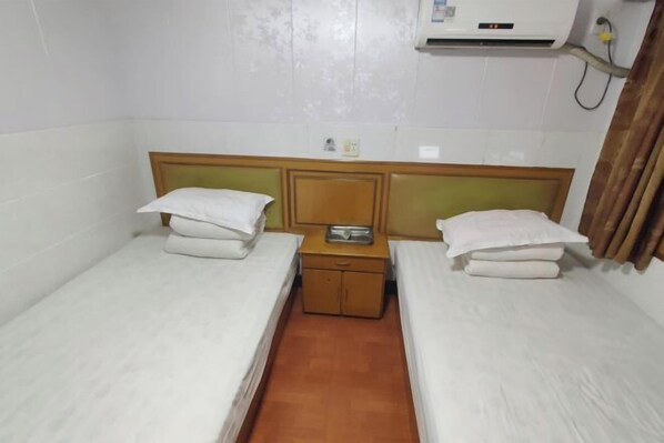 A small, clean room with two single beds, a wooden nightstand, an air conditioning unit, and a wall-mounted shelf. - Jinying Hostel (Shanghai)