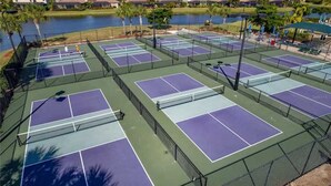A tennis court complex with multiple courts, surrounded by a fence, and near a body of water. - Resort Style 3 Bed/2 Bath Garage Home in GATED River Strand Golf & Country Club! (Bradenton)