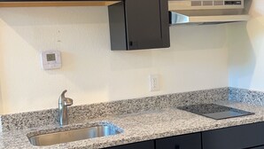 A kitchen with dark cabinets, granite countertops, a stainless steel sink, and a built-in range hood.