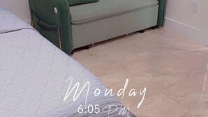 A room with a bed, a green sofa, and a tiled floor.
