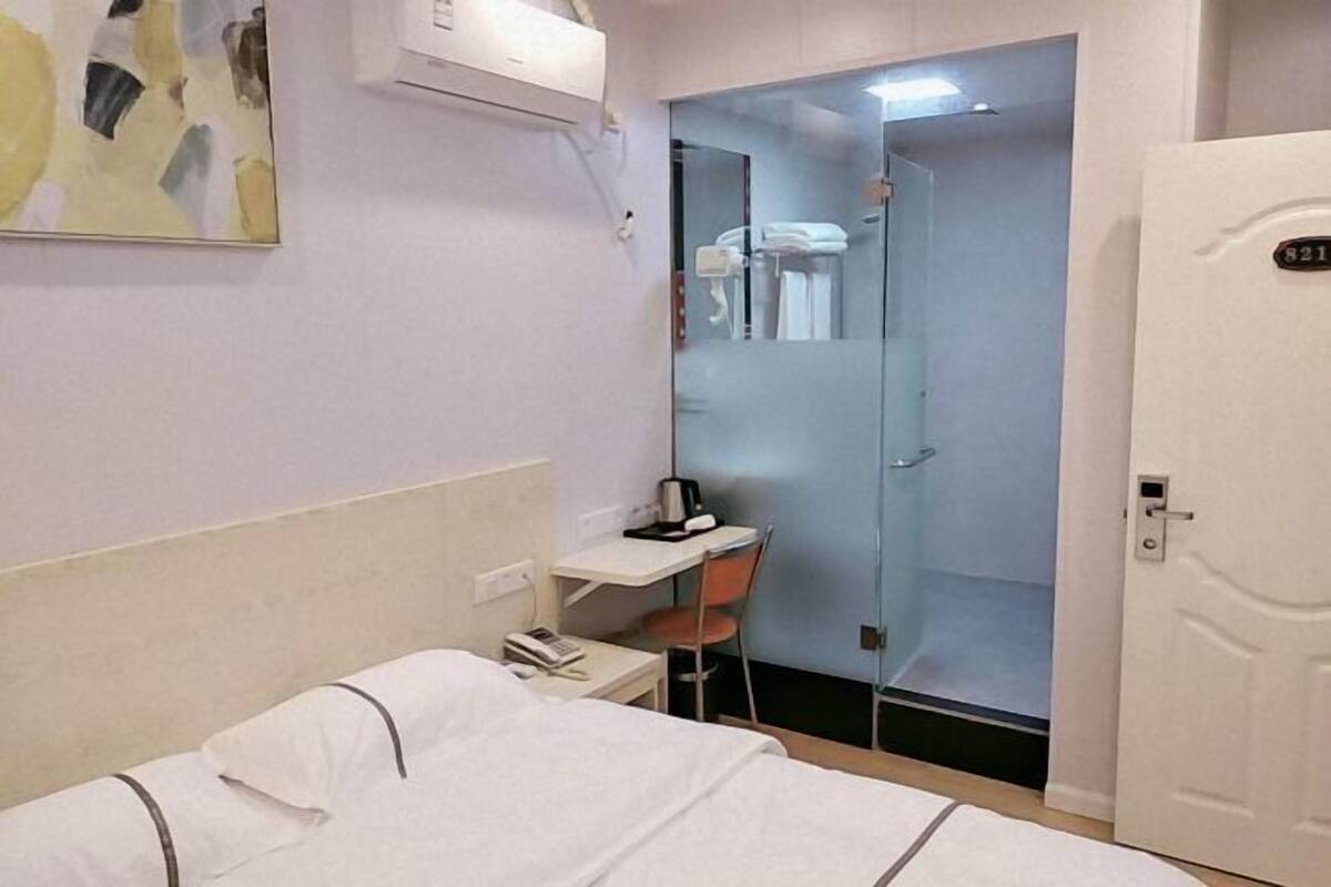 A hotel room with a bed, a desk, a chair, and a shower area.
