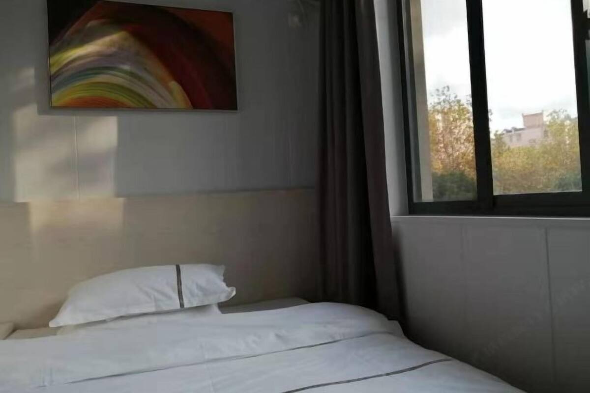A hotel room with a bed, a painting on the wall, and a window with curtains.