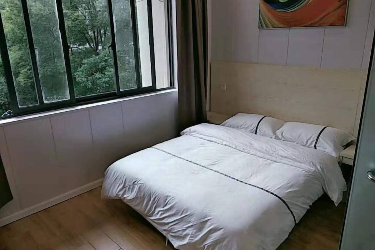 A bedroom with a bed, a window, and a painting on the wall.