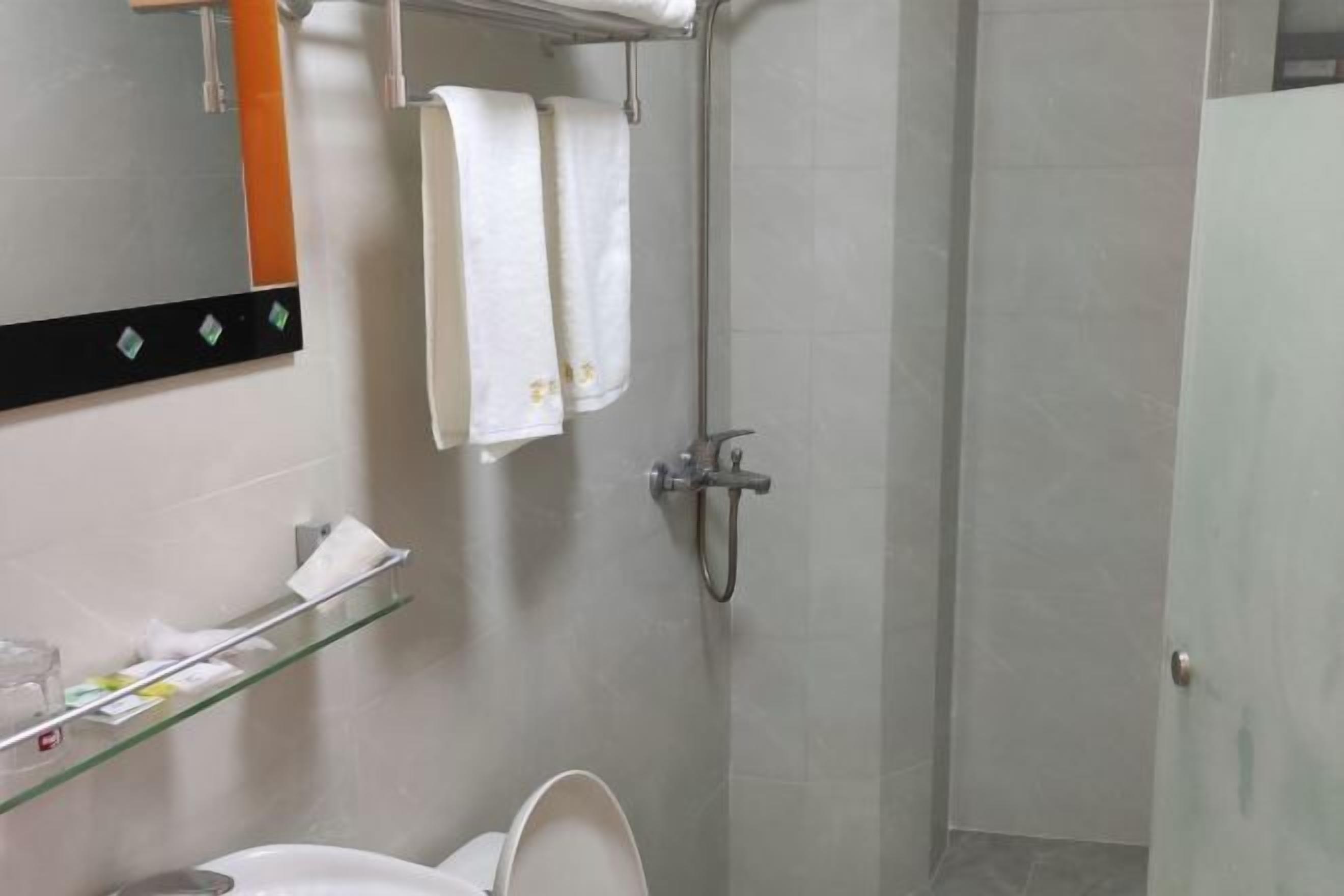 A bathroom with a toilet, a glass shelf with toiletries, a towel hanging on a rack, and a shower area.