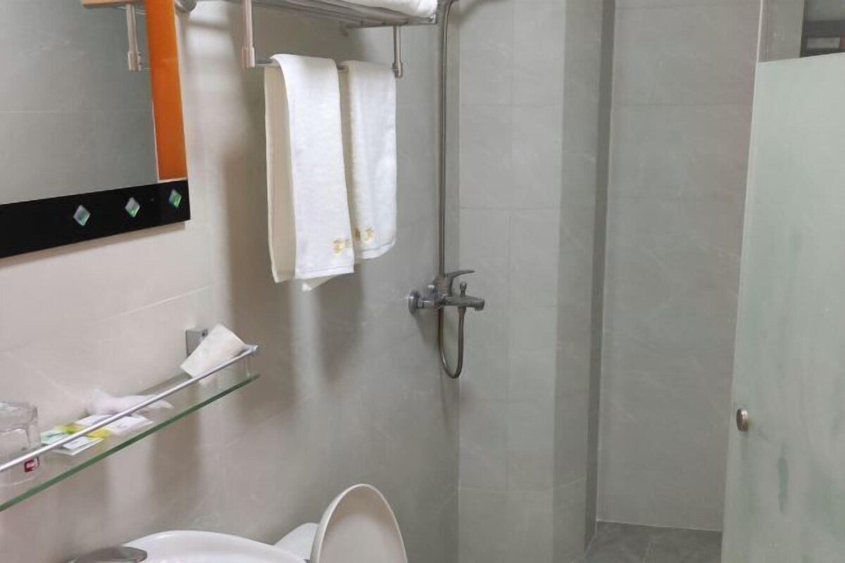 A bathroom with a toilet, a glass shelf with toiletries, a towel hanging on a rack, and a shower area.