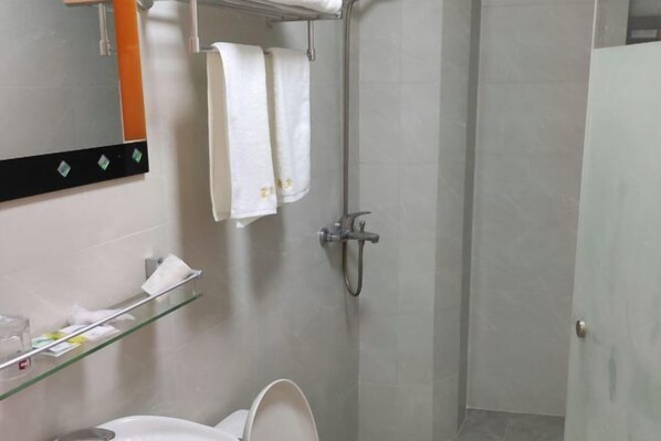 A bathroom with a toilet, a glass shelf with toiletries, a towel hanging on a rack, and a shower area. - Xiangfu Hotel (Shanghai Guoding Road) (Shanghai)