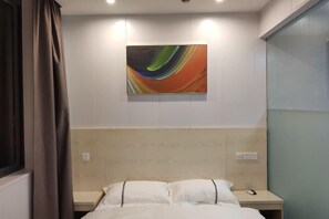 Habitación de hotel con cama, mesita de noche, un cuadro abstracto colgado en la pared y ventana con cortinas.
