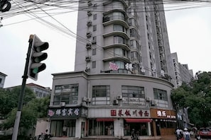 A multi-story building with a curved facade, several commercial establishments on the ground floor, and a traffic light in the foreground. - Xiangfu Hotel (Shanghai Guoding Road) (Shanghai)