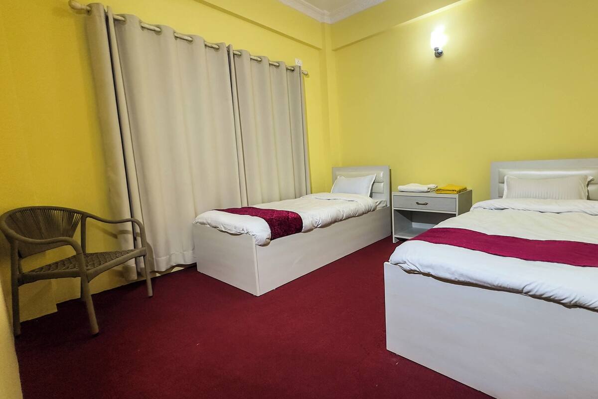 Habitación de hotel con dos camas, un escritorio, una silla y una ventana con cortinas.