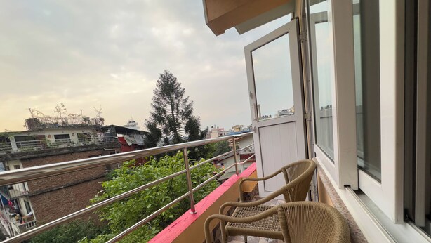 Ein Balkon mit Korbstühlen, einem Metallgeländer und Blick auf Gebäude und Grünflächen darunter.