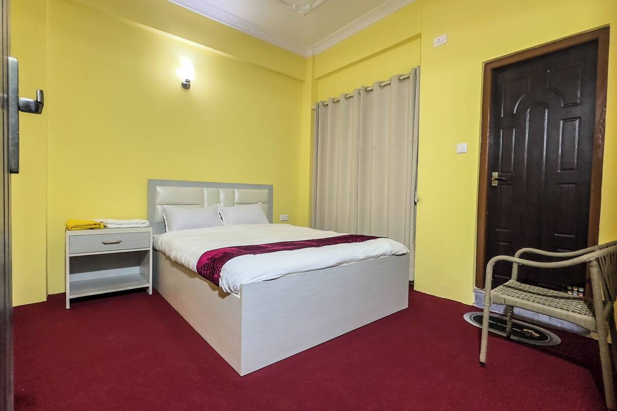 Una habitación de hotel con una cama, una mesita de noche, una silla, una puerta y una lámpara.