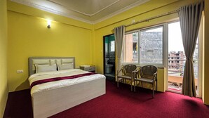 Ein Hotelzimmer mit einem Bett, zwei Stühlen, einem fenster mit Vorhängen und Blick auf Gebäude.