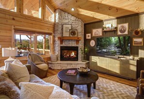 Een knus interieur van een chalet met een stenen openhaard, houten wanden, een televisie en een comfortabele zithoek.