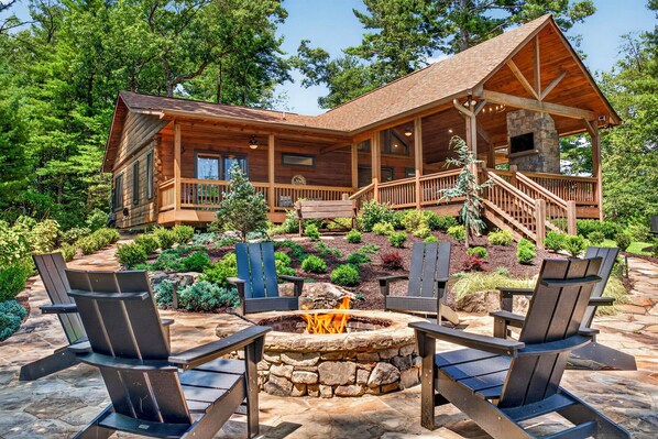 A log cabin with a stone fireplace, outdoor seating, and a covered porch.