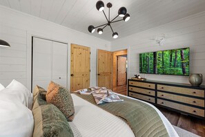 Ein Schlafzimmer mit einem Bett, Kissen, einem Schminktisch, einem Fernseher und einer Deckenleuchte.
