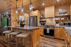 A modern kitchen with wooden cabinets, a stainless steel refrigerator, a built-in oven, and a granite countertop.