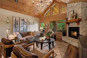 A cozy log cabin interior with a fireplace, wooden furniture, and framed artwork.