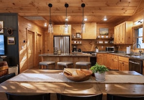 A wooden cabin interior with a kitchen featuring a central island, bar stools, a refrigerator, and a sink.